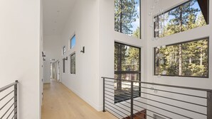 A modern interior with a wooden floor, white walls, and large windows offering views of a forest.
