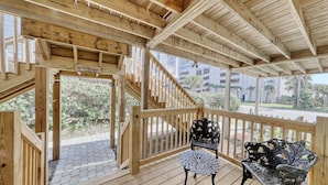 Una terraza de madera con una escalera que conduce a un espacio cubierto, dos sillas de metal ornamentadas y un letrero que dice "TO THE SEA SHORE".