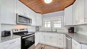Una cocina moderna con armarios blancos, un microondas de acero inoxidable, una estufa negra y una ventana con vistas.