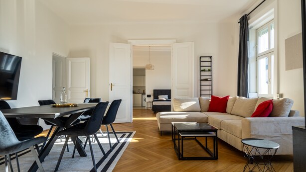 A modern living room with a dining area, a sofa with red cushions, and a TV on the wall. - Rochus Stylish Stays (Vienna)
