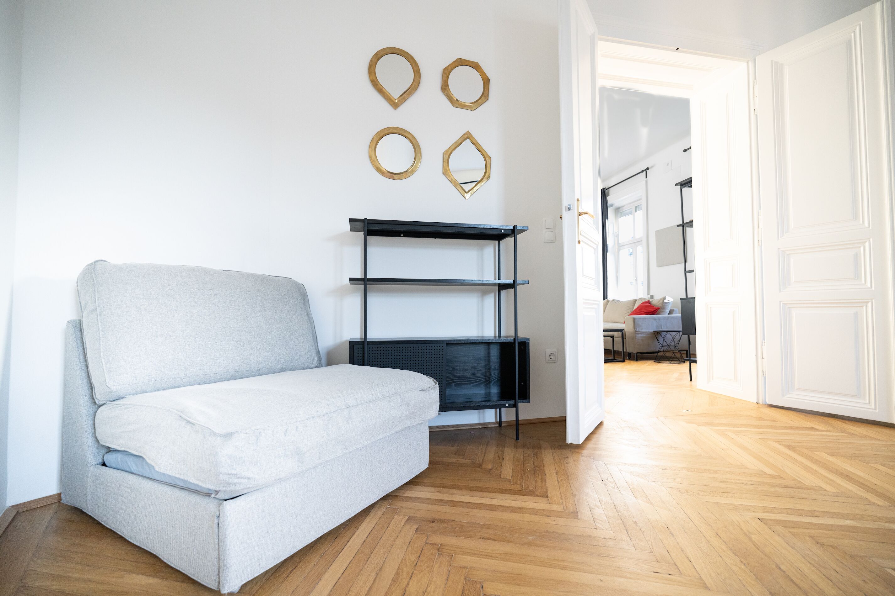 A modern living room with a grey sofa, a black shelving unit, and a wooden floor.