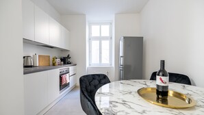 A modern kitchen with white cabinets, a marble countertop, a black upholstered chair, and a dining table with a bottle of wine. - Rochus Stylish Stays (Vienna)