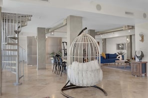 A spacious living area with a modern staircase, a hanging chair with white fur, a blue sofa, and a coffee table.