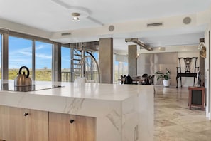A modern kitchen with a marble countertop, a kettle, and a dining area with chairs and a table.