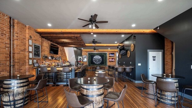 A bar area with wooden barrels as tables, bar stools, and a counter with bottles. - *New* Monmouth Loft 1 | City Chic 1 BDR (Newport)