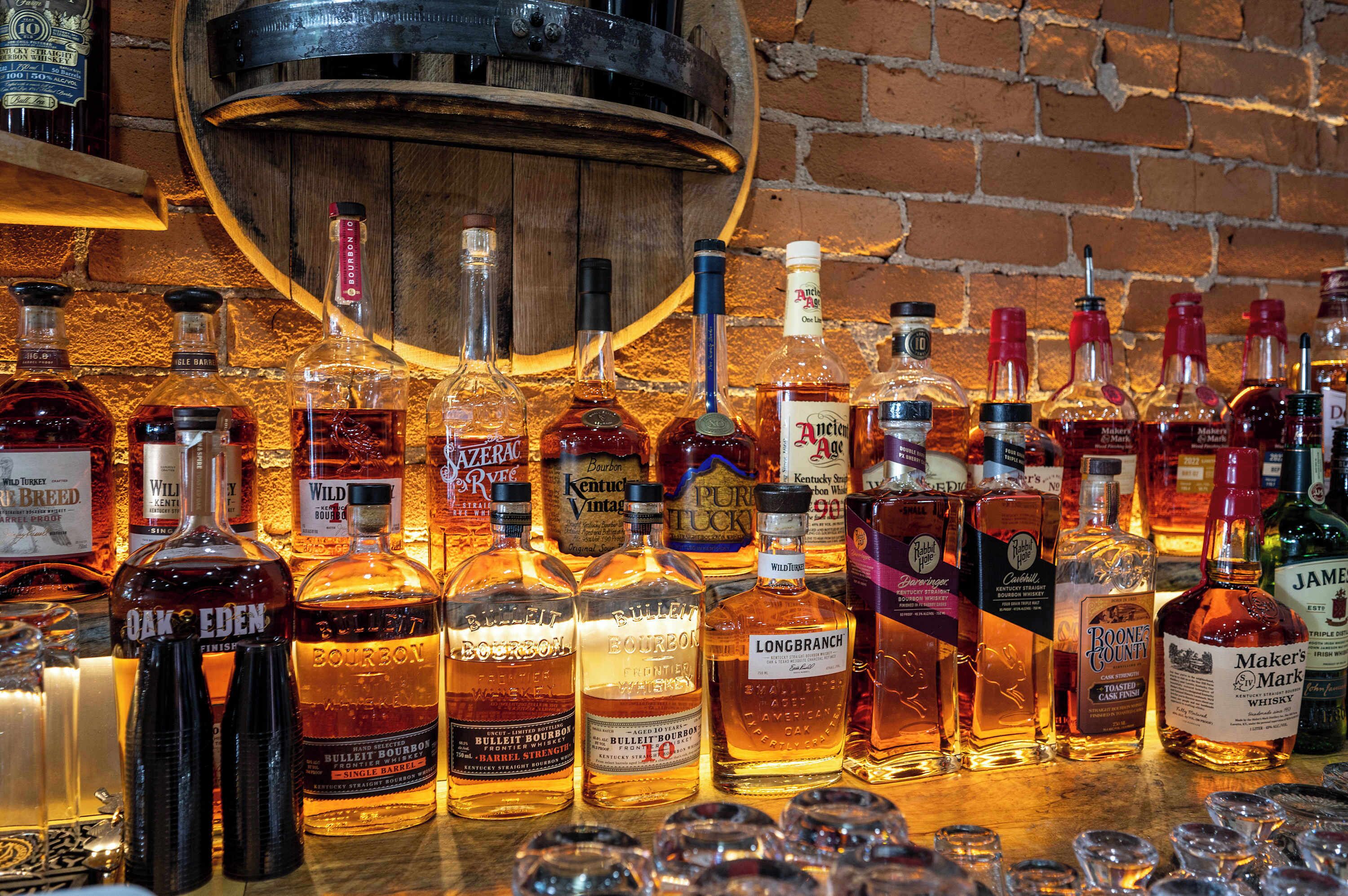 A variety of whiskey bottles displayed on a wooden surface with a brick wall in the background.