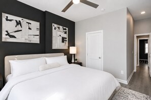 Une chambre à coucher avec un lit, une table de chevet, une lampe et des œuvres d’art abstraites accrochées au mur.