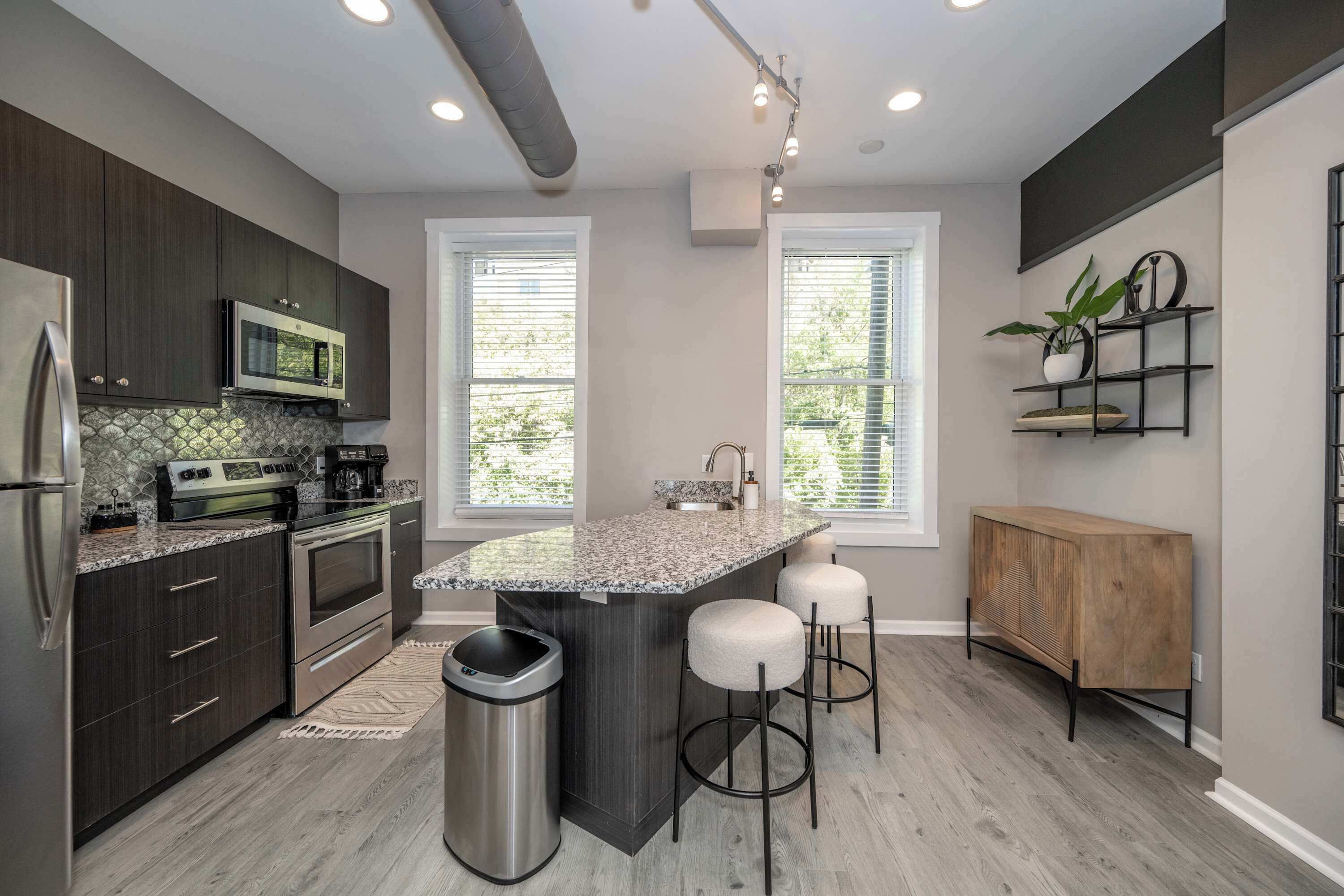 A modern kitchen with dark cabinets, stainless steel appliances, a granite countertop, and a central island with bar stools.