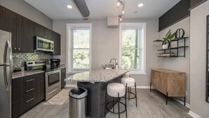Una cocina moderna con armarios oscuros, electrodomésticos de acero inoxidable, encimera de granito y una isla central con taburetes de bar.