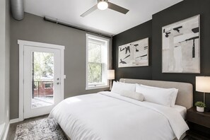 Une chambre à coucher avec un lit, un ventilateur de plafond, une porte et deux fenêtres.