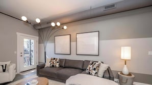 Una sala de estar moderna con un sofá gris, un sillón blanco, una mesa de centro de madera y una lámpara en una mesita auxiliar.