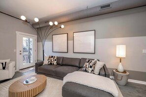 A modern living room with a grey sofa, a white armchair, a wooden coffee table, and a lamp on a side table.