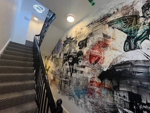 Un escalier recouvert d’une moquette à motifs et un mur orné d’une fresque représentant l’emblème d’un club de football et un oiseau.