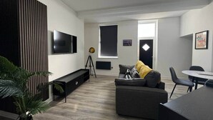A modern living room with a flat-screen TV, a sofa, a dining table, and a potted plant.