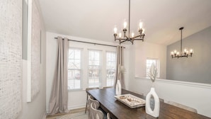 A dining area with a wooden table, chairs, a chandelier, and a view of the outside through large windows. - Walton Arkside Oasis (Walton)