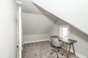 Une petite pièce inclinée, avec un bureau, une chaise et une porte.