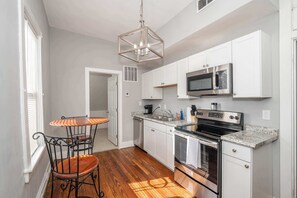 A modern kitchen with white cabinets, a stainless steel stove, and a granite countertop. - Suites on Main 3 (Covington)