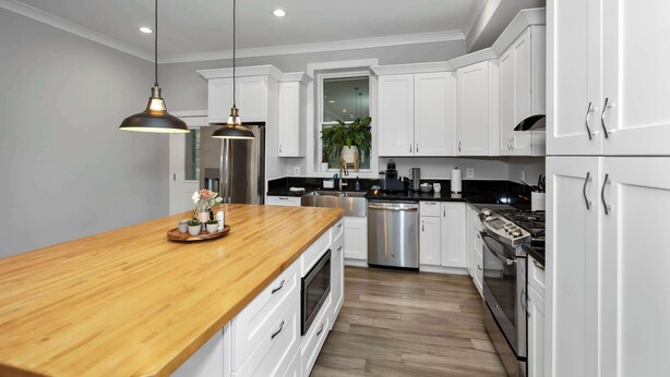Une cuisine moderne avec des meubles blancs, un plan de travail en bois, des appareils en acier inoxydable et des luminaires suspendus.