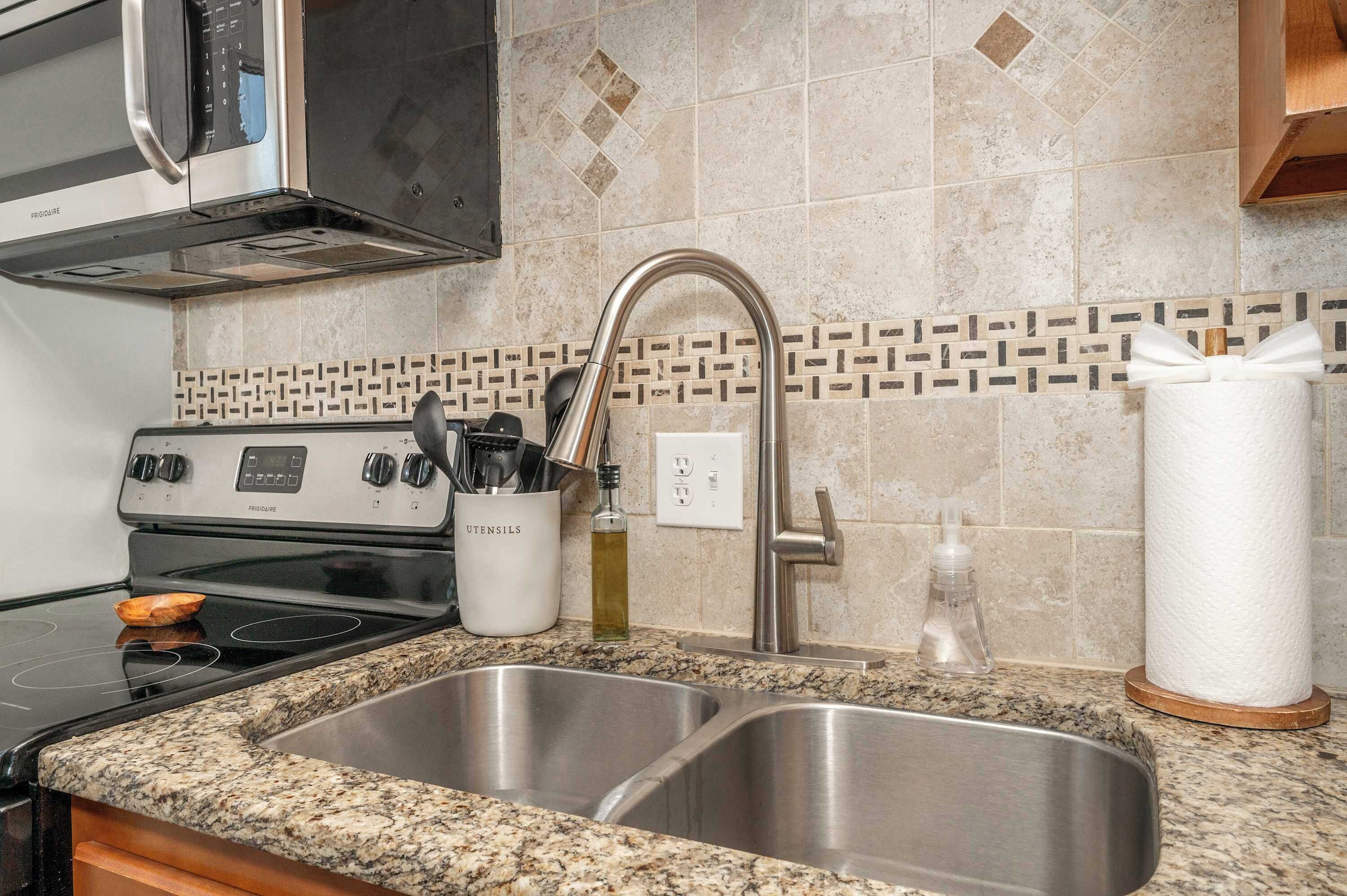 A kitchen with a stainless steel sink, a stove, and a microwave.
