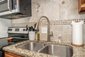 Cocina con pileta de acero inoxidable, estufa y microondas. Se observa un organizador de utensilios y un dispensador de toallas de papel.