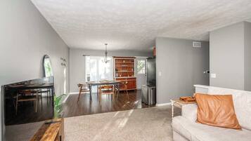 A spacious living room with a dining area, a kitchen, and a white sofa with an orange pillow.
