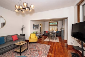 A living room with a sofa, armchair, coffee table, and a TV. There is a dining area with a table and chairs. - Historic 4BR | Walk Bellevue | 5 Min to Cincy (Dayton)