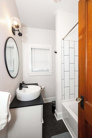 A bathroom with a white sink, black countertop, a mirror, a window, and a wooden door.