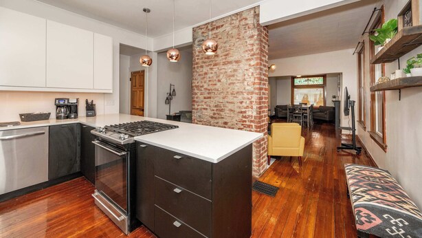 A modern kitchen with a central island, stainless steel appliances, and a brick accent wall. - Historic Retreat Gateway (Dayton)