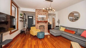 A living room with a fireplace, a sofa, a TV, and a wooden floor. - Historic Retreat Gateway (Dayton)