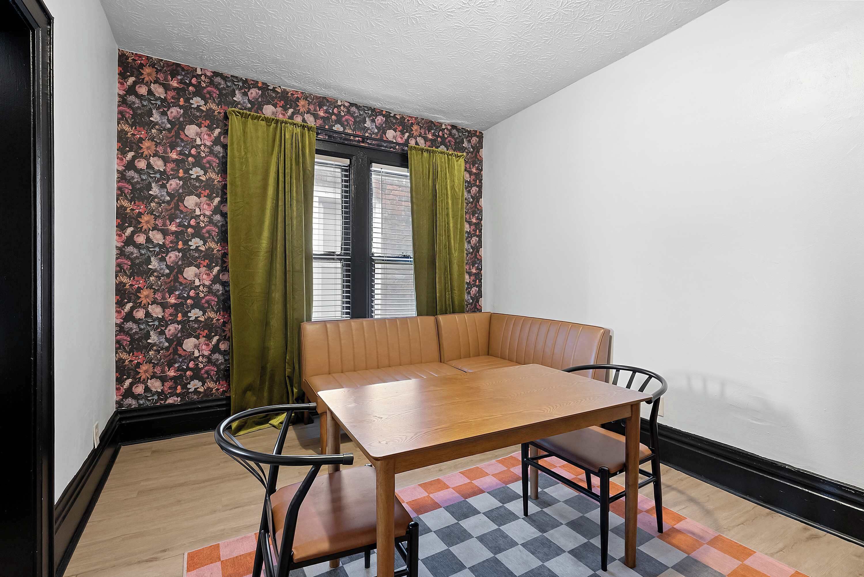 Ein Zimmer mit Holztisch, Bank, Wand mit Blumenmuster und Schachbrettmusterteppich.