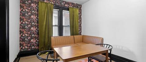 Ein Zimmer mit Holztisch, Bank, Wand mit Blumenmuster und Schachbrettmusterteppich.