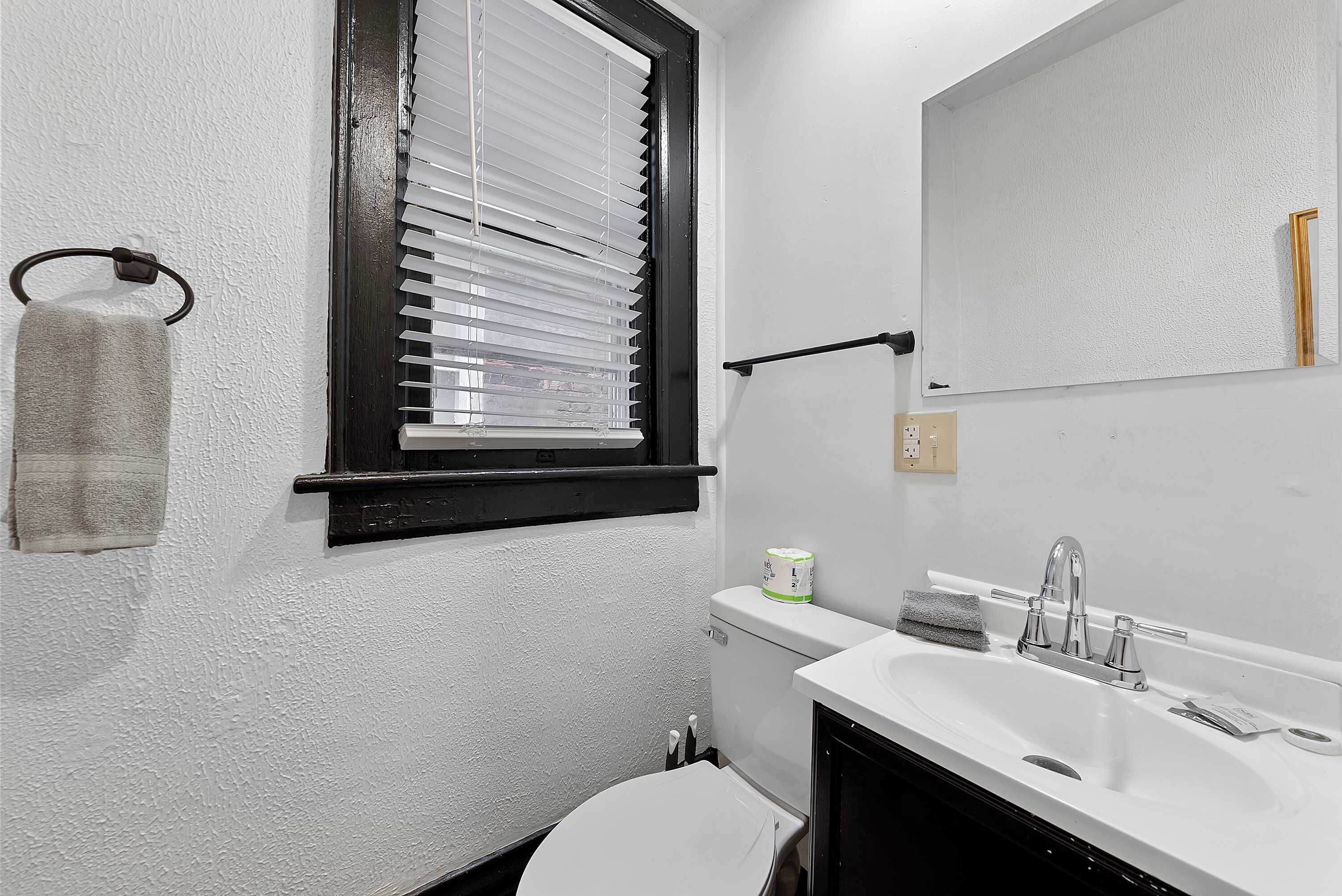 A small bathroom with a white sink, a mirror, a toilet, and a window with blinds.