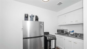 A modern kitchen with a stainless steel refrigerator, a black stove, and white cabinets. - Northside Suites 3 – A Chic, Relaxed Stay for 2 (Cincinnati)