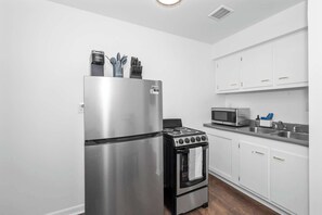 A compact kitchen with a stainless steel refrigerator, a black stove, a microwave, and white cabinets. - Northside Suites 3 – A Chic, Relaxed Stay for 2 (Cincinnati)