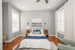 A bedroom with a bed, two bedside tables, a ceiling fan, a window with blinds, and a wall-mounted artwork. - Findlay Market | 2 Ensuites + Parking (Cincinnati)