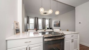 A modern kitchen with white cabinetry, a built-in oven, and a dining area with a glass table. - The Heart of Madison 3 (Covington)