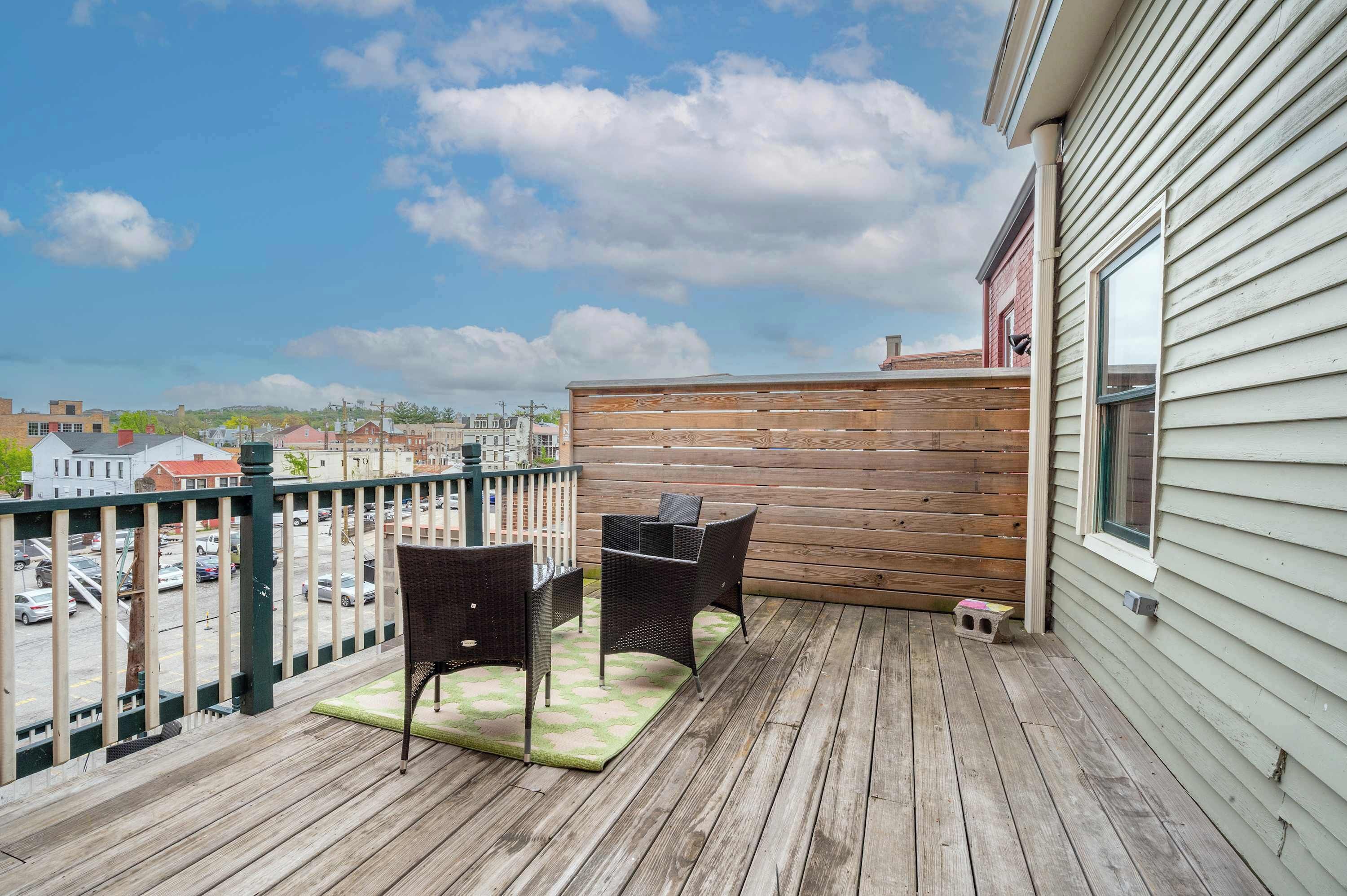 A wooden deck with two wicker chairs and a table, overlooking a street with parked cars and buildings.