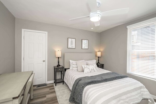 A bedroom with a bed, bedside tables, a ceiling fan, and a window with blinds.
