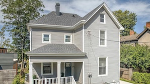 Une maison à deux étages avec un porche à l’avant, une cheminée et un compteur électrique visible.