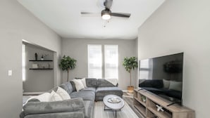 Un salon moderne avec un canapé d’angle, un téléviseur à écran plat et un ventilateur de plafond.