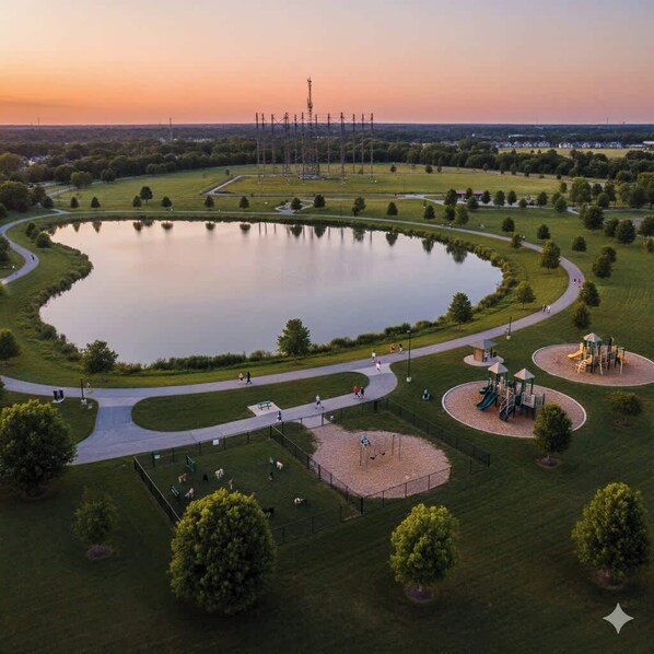 A park with a large pond, walking paths, playgrounds, and a power line tower in the background.