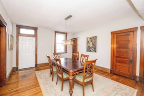 A dining room with a wooden table and chairs, a chandelier, and a patterned rug.