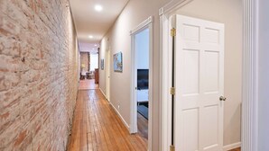 A hallway with a brick wall, wooden flooring, and white doors leading to rooms. - Sweet Escape (Cincinnati)