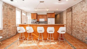 A kitchen with a brick wall, wooden cabinets, a central island with bar stools, and a ceiling fan. - Sweet Escape (Cincinnati)