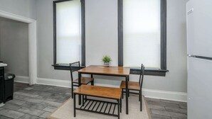 A kitchen with a wooden table and chairs, a refrigerator, and a window with blinds. - Chic, Modern Gem with Style (Cincinnati)