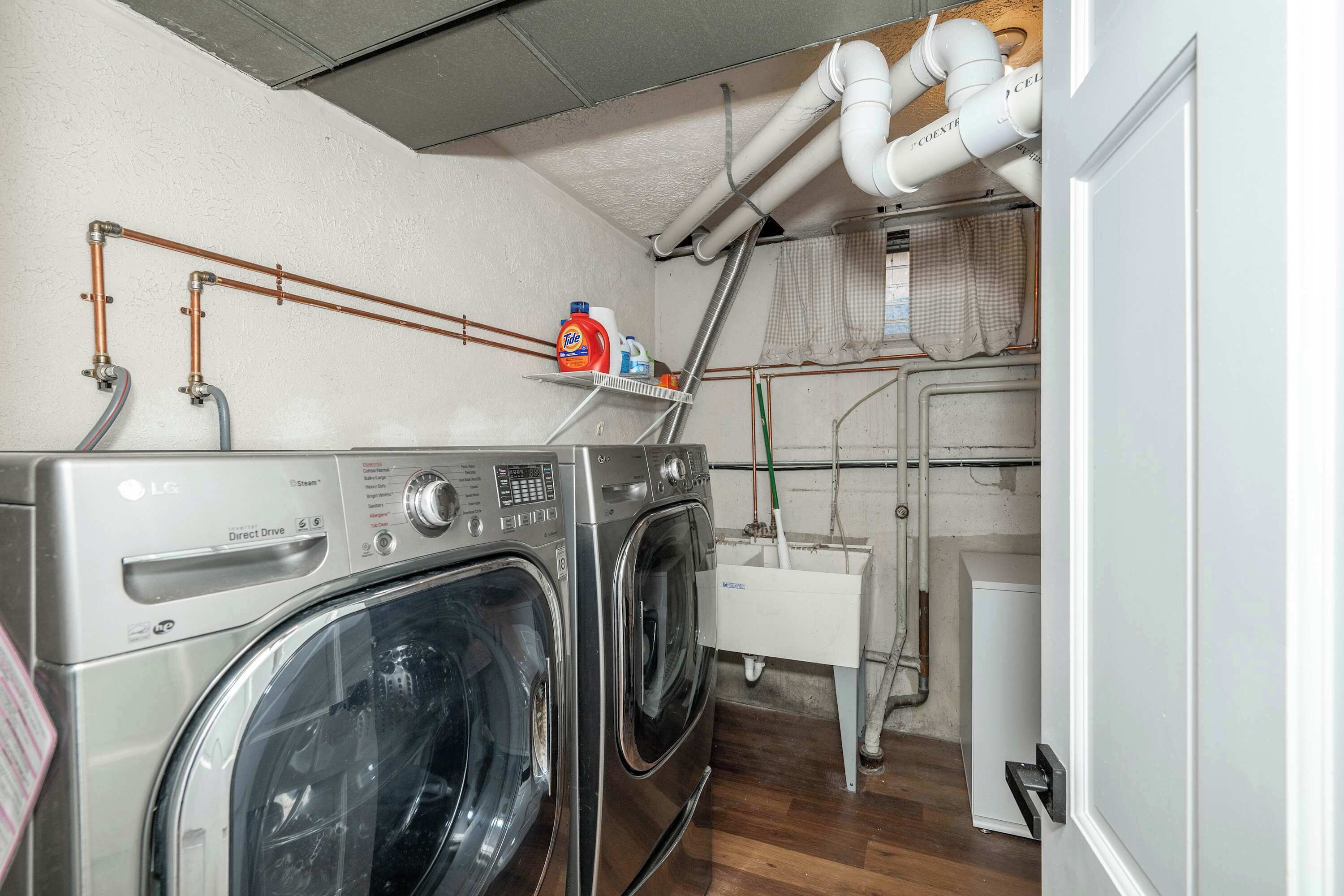 A laundry room with two stacked washers and dryers, a shelf with cleaning supplies, and visible plumbing.