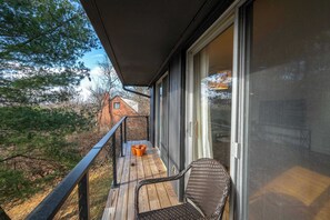 Una terraza de madera con una silla y una maceta, con vistas a un área boscosa y una casa al fondo.