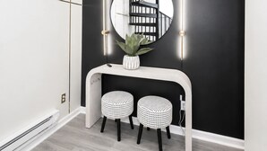 A modern interior with a black wall, a white console table, two black and white stools, a potted plant, and a round mirror with a black and white image. - Queen City Views 2 – Sleeps 2! (Cincinnati)