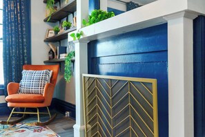 A room with a blue door, a rocking chair with a patterned cushion, and shelves with plants and decorative items.