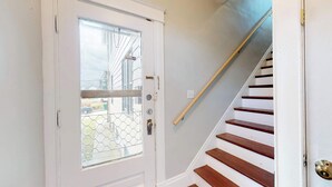 Une porte blanche avec un panneau de verre et une chaîne de sécurité, qui donne sur un escalier en bois avec des murs blancs.